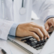 Close up of male doctor typing on laptop computer while sitting at the table. Medical staff