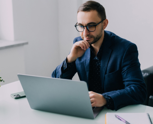 Handsome young business man sitting at his desk in a office with large windows