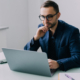 Handsome young business man sitting at his desk in a office with large windows