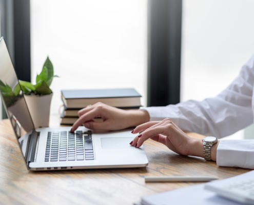 Woman working on laptop computer at table in office. Close up